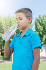 A young boy drinks water from a plastic bottle.