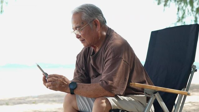 Happy asian senior elderly using smartphone technology outside on the beach having fun enjoy freedom on summer vacation people lifestyle activity on weekend concept.