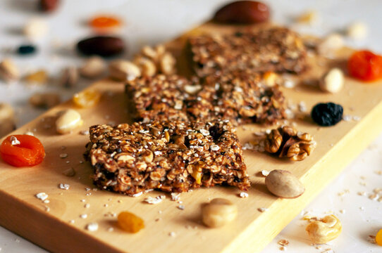 bar with flakes, nuts and dried fruits on light wooden board with ingredients scattered side by side on a gray background. board is located diagonally. natural light source, selective focus, close-up