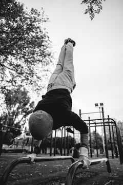 Healthy and fit young latin man with wool cap and wristbands doing calisthenics (inverted pose) on a street workout park with beautiful and sunset sky (in black and white)