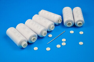 Set of White buttons and Spools threads on a blue background.