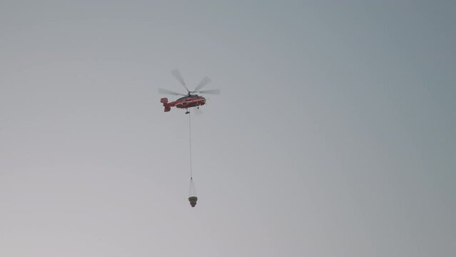 A flying helicopter with cargo . Action . Foggy gray sky with a big red flying helicopter that drops cargo down.