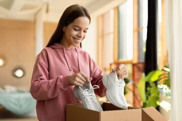 Happy teen girl buyer holding new footwear unpacking cardboard box, receiving shoes after...