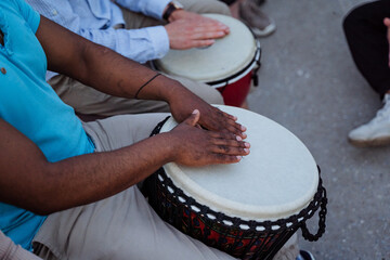 Drumming close-up, a black guy beats the rhythm on a djmba, a street musician performing in front...