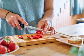 Woman making summer strawberry sandwich. Female hands cutting ripe red strawberry on cutting board....