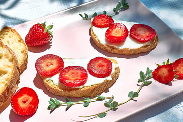 Summer delicious strawberry sandwich. Toast bread with spread stracchino cheese and slices of ripe red strawberry on pink plate on the table in the garden. Healthy eating, fruit dieting brunch.