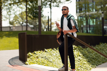 Handsome african american guy using navigator on cellphone or chatting in social networks while walking in urban area