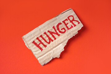 Hunger text written on a piece of cardboard on a red background. Food crisis, global hunger, food...