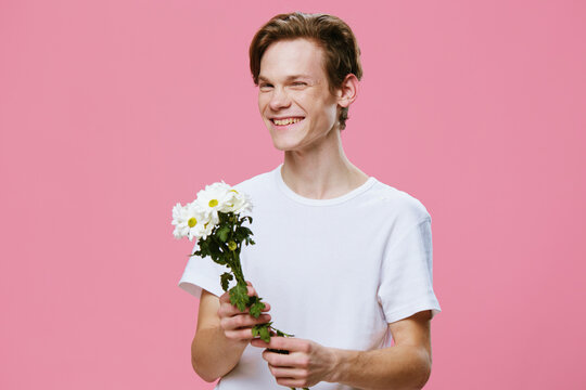 cute, smiling young man in a white t-shirt with daisies in his hands on a pink background with space for text.
