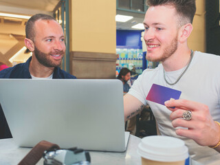 Two smiling young Caucasian boys shopping on the computer with a credit card.