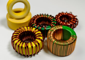 Small family of inductive chokes on a white background. Inductive component, copper wire coil, yellow toroid - macro picture. 