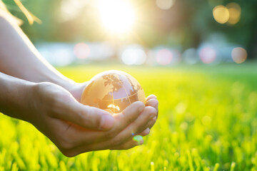 Glass globe in kid hands on blurred green grass banner background with sunlight in city. Concept of...