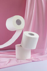 White toilet paper levitate on a pink silk background.  The second roll is worth it.  The third roll falls
