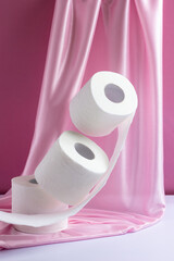 Three rolls of levitating white toilet paper on a pink silk background