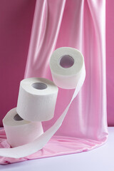 Three rolls of levitating white toilet paper on a pink silk background