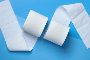
Two rolls of toilet paper lie unwound in different directions on a blue and light blue background.  View from above