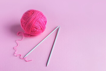 Pink knitted wool on a pink background with knitting needles for knitting warm clothes and hobbies needlework