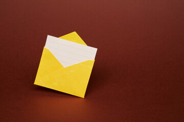 Yellow color paper office envelope with white lined sheet with copy space isolated on the bright solid fond plain dark brown background