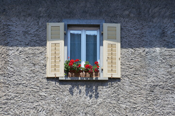Italian window on the rustic grey wall facade with open beige color classic shutters and flowers on...