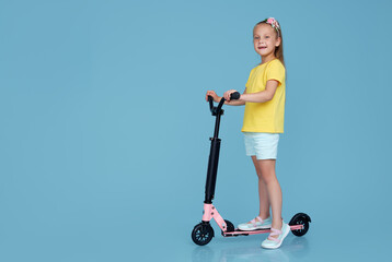 Little child girl in summer clothes on scooter isolated on blue wall background, children studio portrait. People, childhood lifestyle concept. © oes