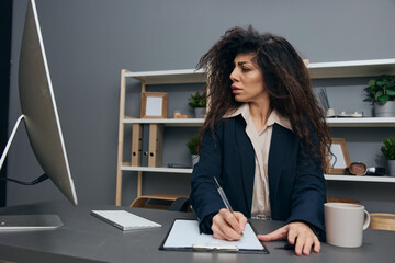 Focused interested attentive tanned curly Latin businesswoman in jacket undergo professional development in office. Copy space Mockup Banner. Corporation leader lady uses modern computer in work