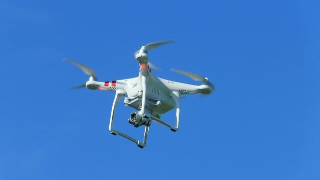 White quadcopter fly in the blue sky. Drone is flying high over the terrain.