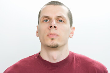 A confident man in a red t-shirt looks straight on a white background.  Modern. Studio. White. Young. Casual. Fashion. Lifestyle. Authority. Concentration. Hold