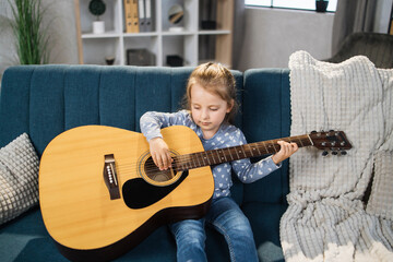 Beautiful young charming little girl smiling while playing classic guitar at home. Caucasian...