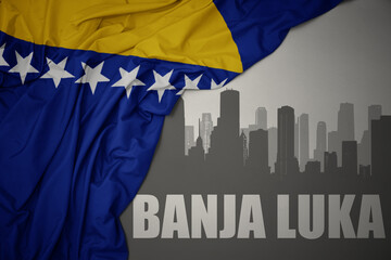 abstract silhouette of the city with text Banja Luka near waving national flag of bosnia and herzegovina on a gray background.