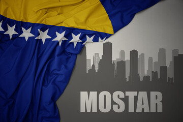 abstract silhouette of the city with text Mostar near waving national flag of bosnia and herzegovina on a gray background.