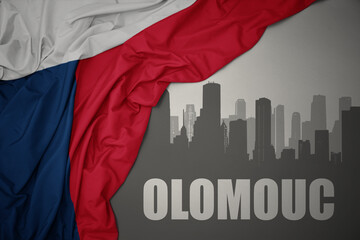abstract silhouette of the city with text Olomouc near waving national flag of czech republic on a gray background.