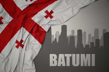 Fototapeta premium abstract silhouette of the city with text Batumi near waving national flag of georgia on a gray background.