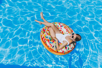 Summer vacation. Tanned woman in glasses in a white swimsuit on an inflatable ring in the pool