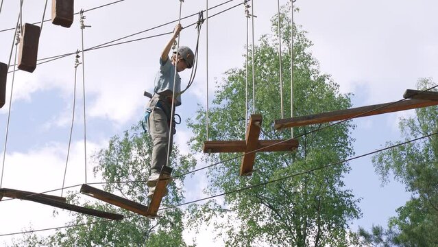 Brave teenage girl overcomes difficult obstacles while walking along a rope stretched between tall trees in a rope town