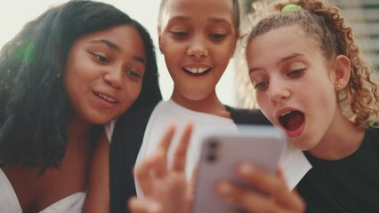 Three girls friends pre-teenage are sitting on the waterfront using mobile phone, watching videos, photos. Three teenagers on the outdoors in urban cityscape background