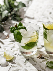 Two summer cocktails with lime and basil in glasses close up on white printed tile
