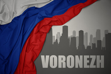 abstract silhouette of the city with text Voronezh near waving national flag of russia on a gray background.
