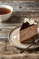 Chocolate cheesecake slice glazed with almond petals topping and tea cup on wooden background