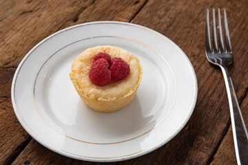 Red raspberry tart on a white plate with a fork on a wooden table - Powered by Adobe
