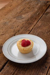 Red raspberry tart on a white plate with a wooden table background