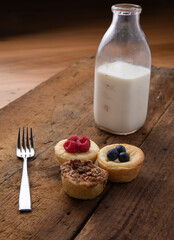 Blueberry, red raspberry, and pecan tarts on a wooden table with a fork and a jar of milk