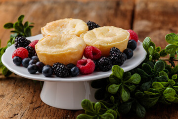 Yellow cream tarts on a plate display with assorted berries and greenery