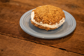 Oatmeal cream cookie on a small blue plate on a wooden table, closeup view