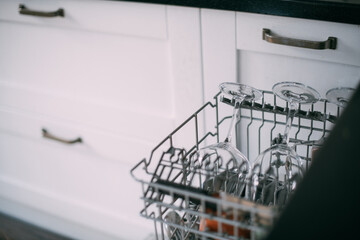Open dishwasher with clean dishes in a white kitchen. Clean glasses, plates, mugs in the dishwasher...