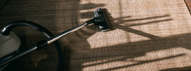 House cleaning. Vacuum cleaner standing on jute carpet in sunlight