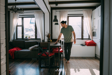 A young man is cleaning, dusting the table in the kitchen and living room at home.
