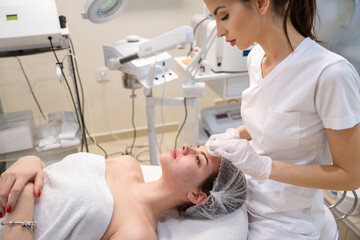 Beautician cleaning the skin of a young woman using cotton discs, finishing her facial treatment in beauty salon.