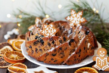 Traditional christmas sweet food: homemade cake with raisins, nuts, fruits decorated with gingerbread cookies. Wooden background, fir tree branches, fairy lights