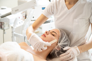 Obraz premium Beautician applying hydro gel mask on the young woman face, before laser treatment in beauty salon.