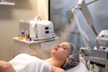 Beautiful woman on ozone therapy with facial steamer in beauty salon. - obrazy, fototapety, plakaty